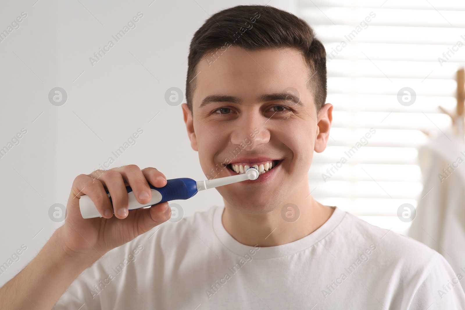 Photo of Man brushing his teeth with electric toothbrush in bathroom