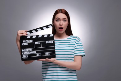 Photo of Shocked actress with clapperboard on grey background. Film industry