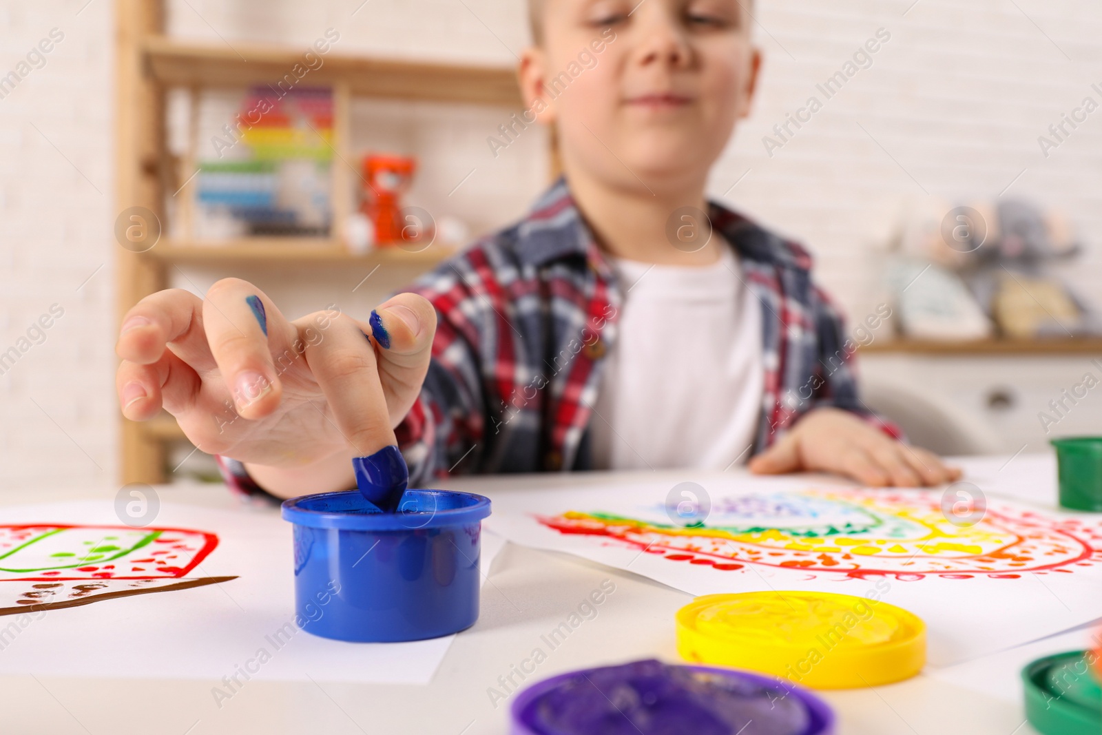 Photo of Little boy painting with finger at white table indoors, focus on hand