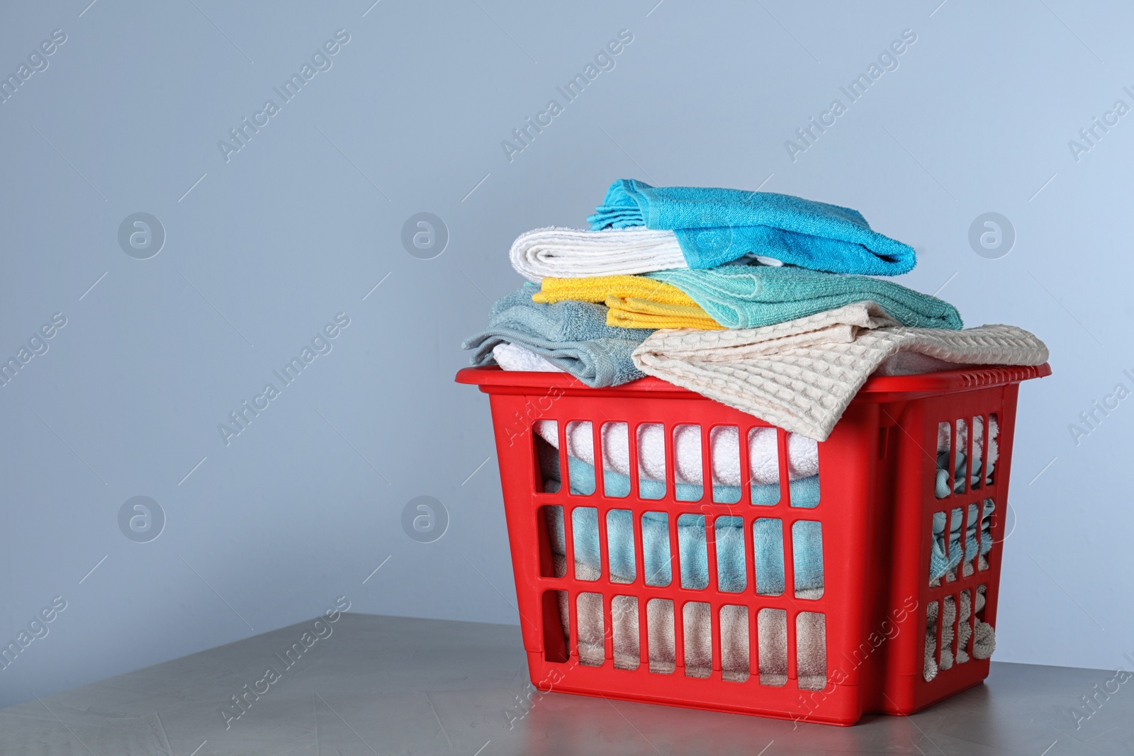 Photo of Plastic laundry basket with clean towels on table against color background. Space for text