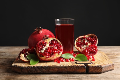 Glass of pomegranate juice and fresh fruits on wooden board against black background