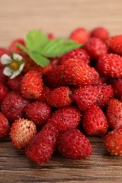 Photo of Pile of wild strawberries, flower and leaves on wooden table, closeup