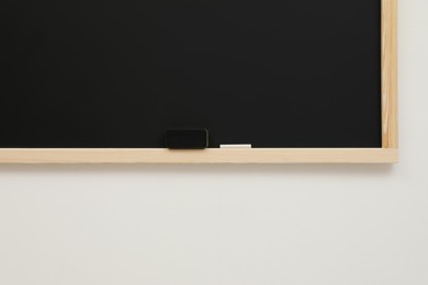 Photo of Clean blackboard with chalk and duster hanging on white wall