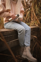 Photo of Woman with thermos sitting on wooden pier among reeds, closeup