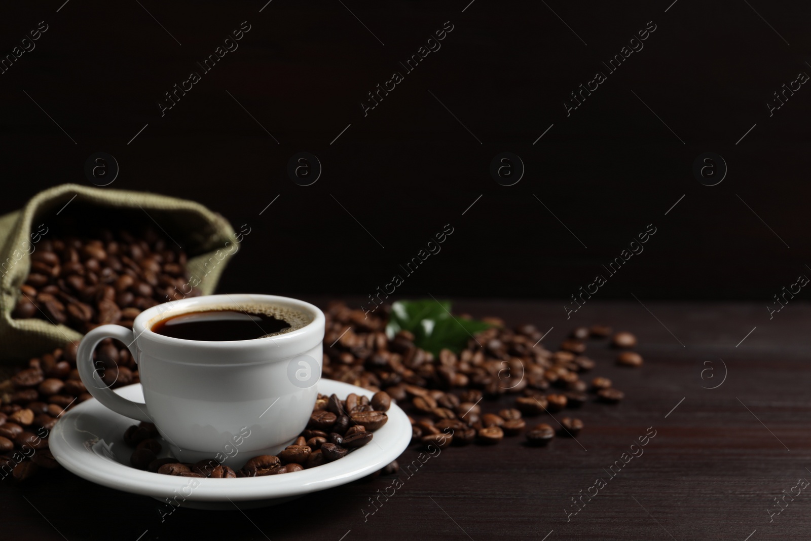 Photo of Cup of aromatic coffee and beans on wooden table. Space for text