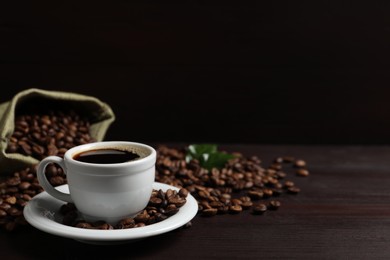 Photo of Cup of aromatic coffee and beans on wooden table. Space for text