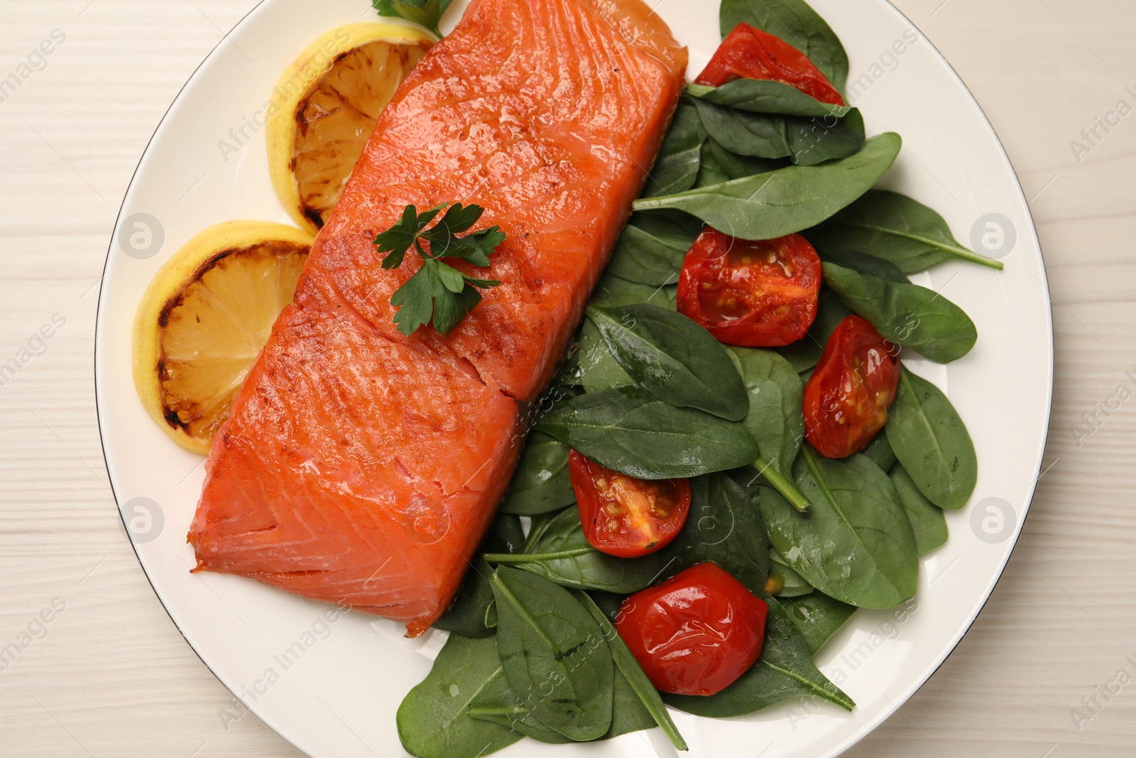 Photo of Tasty grilled salmon with basil, tomatoes and lemon on white wooden table, top view