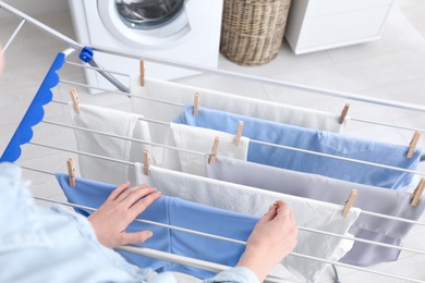 Woman hanging clean laundry on drying rack indoors, closeup