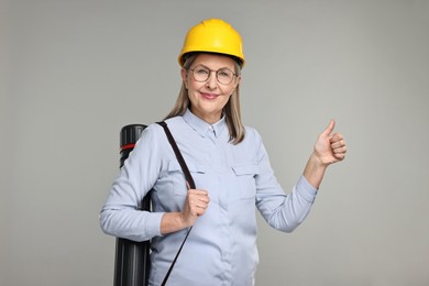 Photo of Architect in hard hat with tube showing thumbs up on grey background