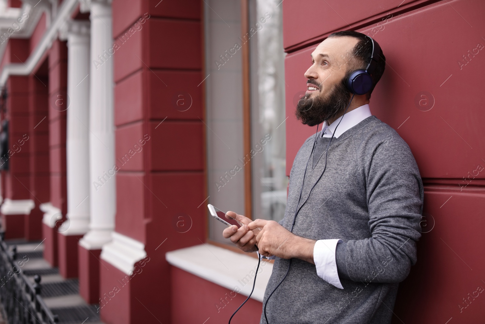 Photo of Mature man with headphones listening to music outdoors. Space for text