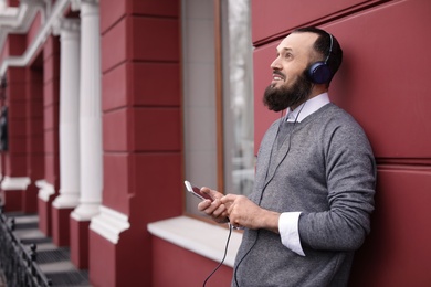 Photo of Mature man with headphones listening to music outdoors. Space for text