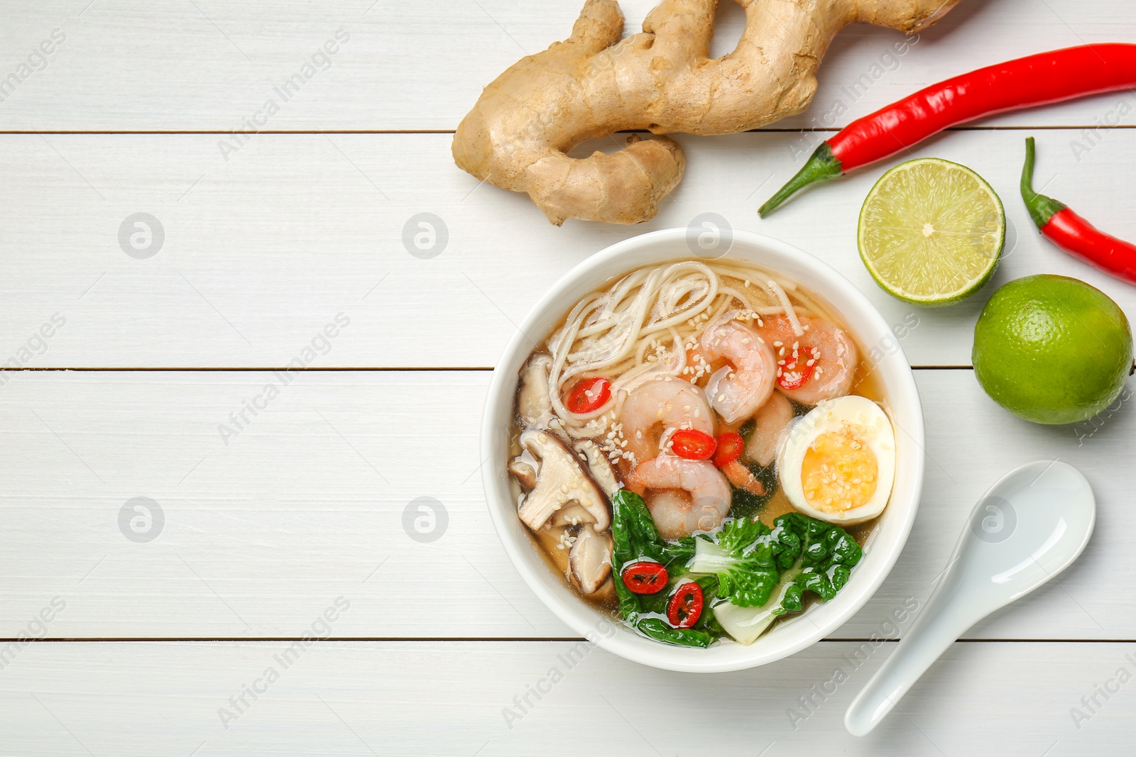 Photo of Tasty ramen with shrimps in bowl and ingredients on white wooden table, flat lay. Space for text