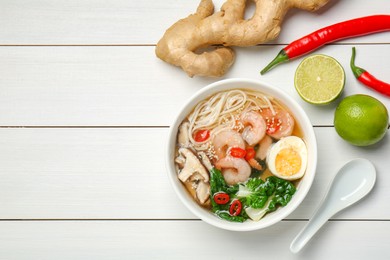 Tasty ramen with shrimps in bowl and ingredients on white wooden table, flat lay. Space for text