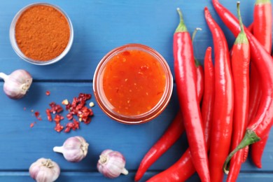 Photo of Spicy chili sauce in jar and ingredients on blue wooden table, flat lay