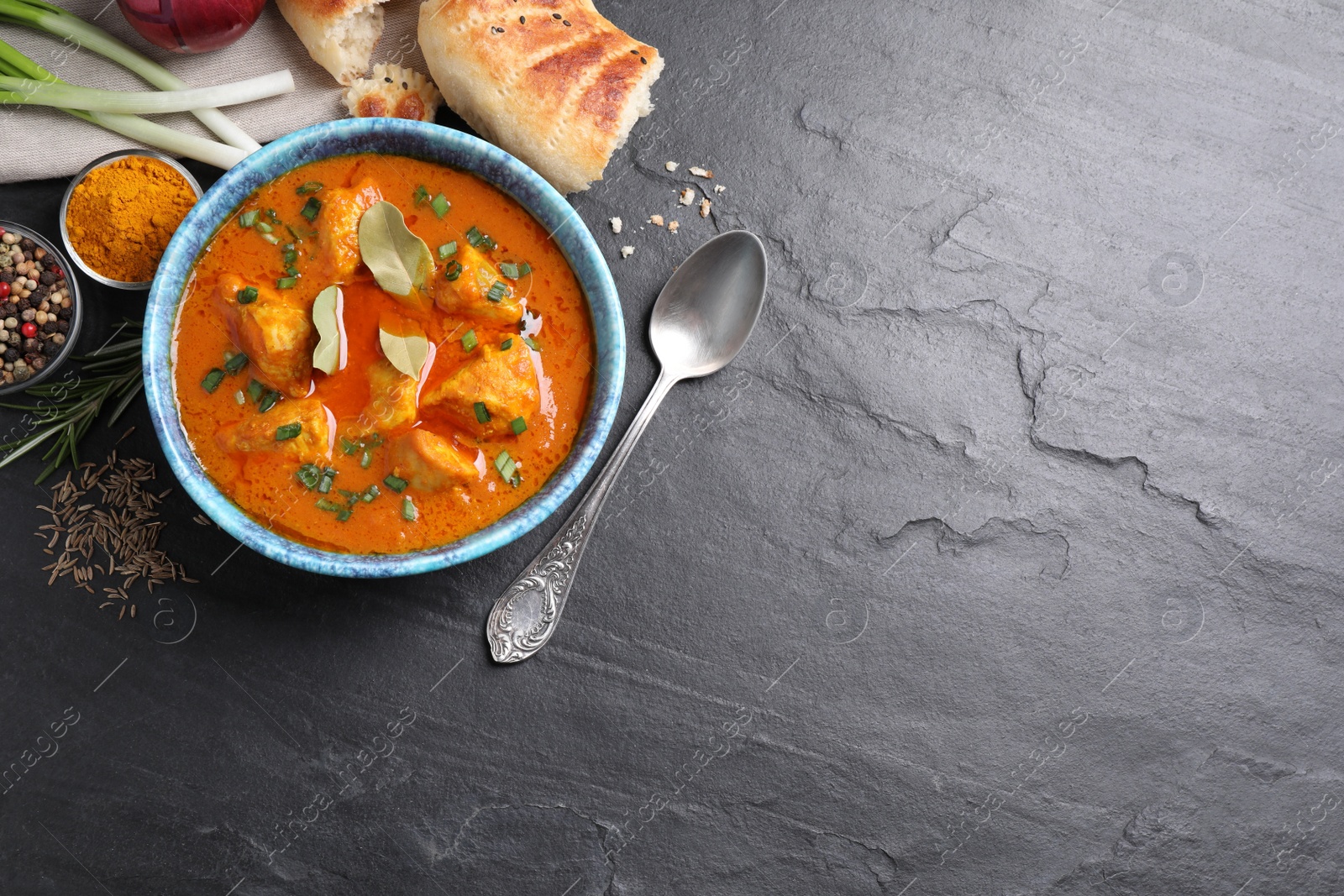 Photo of Bowl of delicious chicken curry on black table, flat lay. Space for text