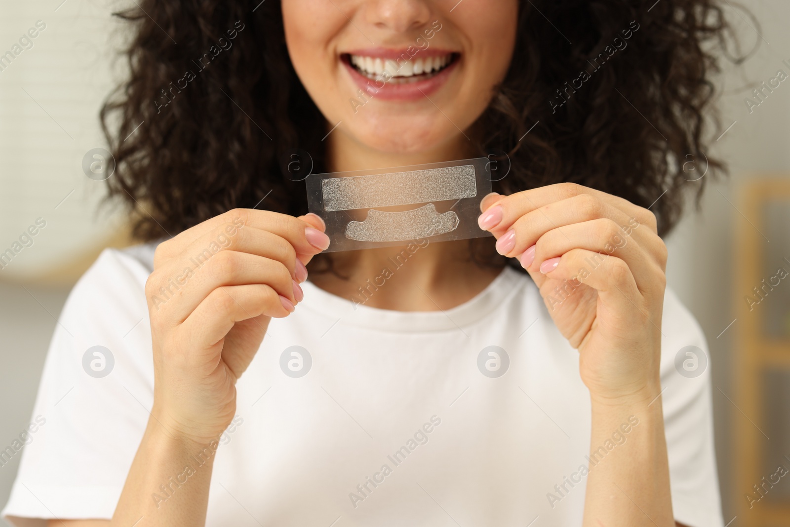 Photo of Young woman holding teeth whitening strips indoors, closeup