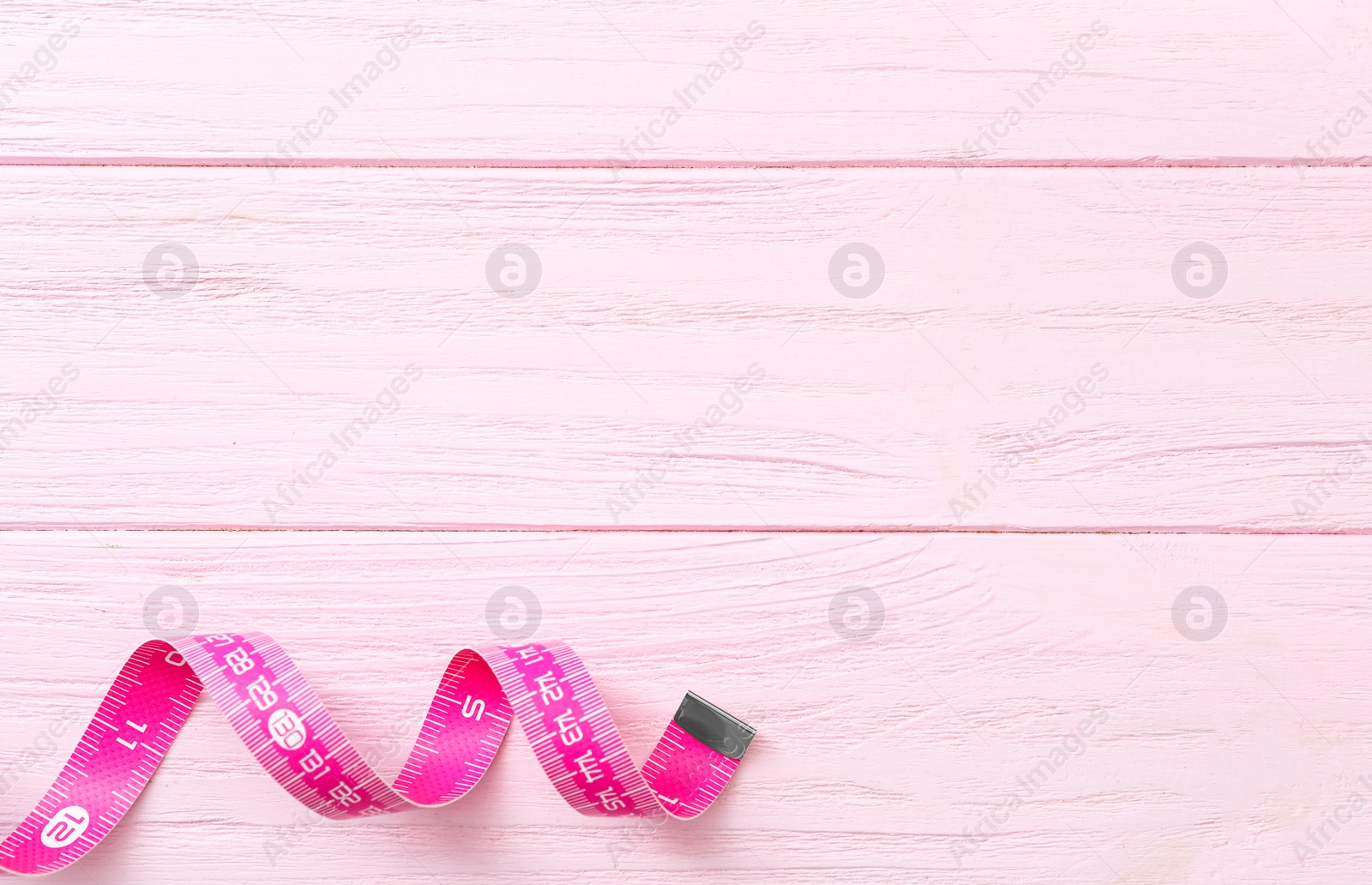 Photo of Measuring tape on pink wooden table, top view. Space for text