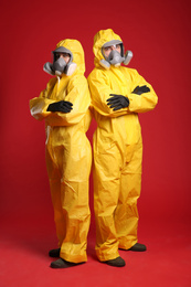 Man and woman wearing chemical protective suits on red background. Virus research