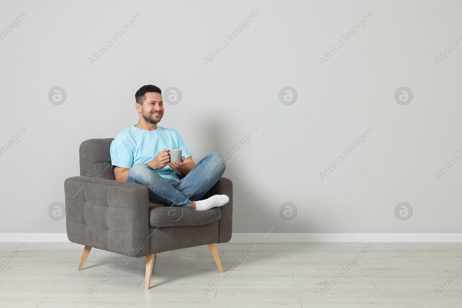 Photo of Happy man with cup of drink sitting in armchair indoors, space for text