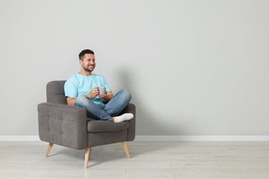 Photo of Happy man with cup of drink sitting in armchair indoors, space for text