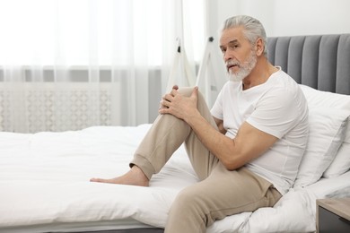 Arthritis symptoms. Man suffering from pain in knee on bed at home