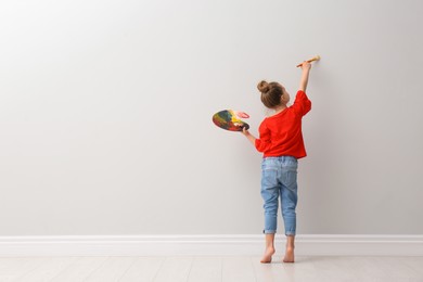 Little girl painting on light grey wall indoors, back view. Space for text