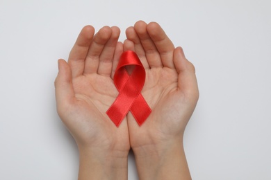 Photo of Little girl holding red ribbon on white background, top view. AIDS disease awareness