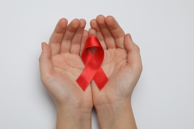 Little girl holding red ribbon on white background, top view. AIDS disease awareness