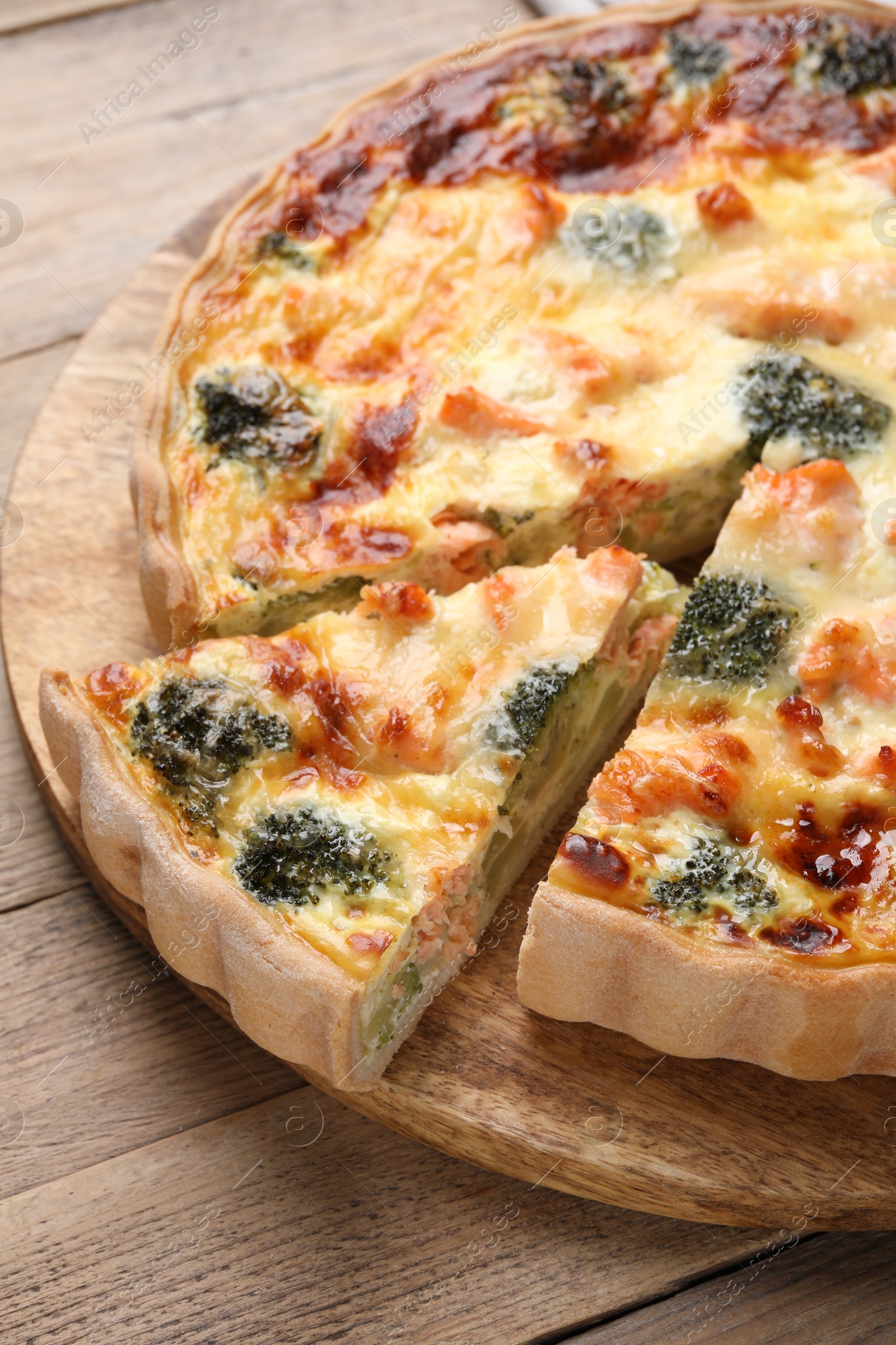 Photo of Pieces of delicious homemade quiche with salmon and broccoli on wooden table