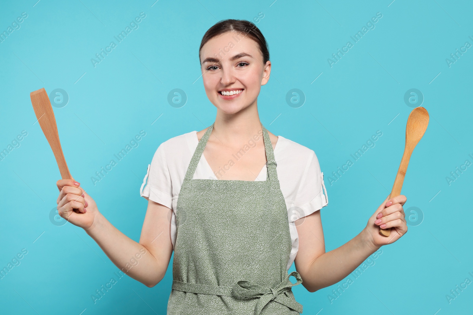 Photo of Beautiful young woman in clean apron with kitchen tools on light blue background