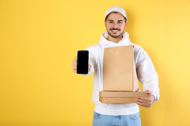 Young man holding orders and smartphone on color background, mockup for design. Online food delivery