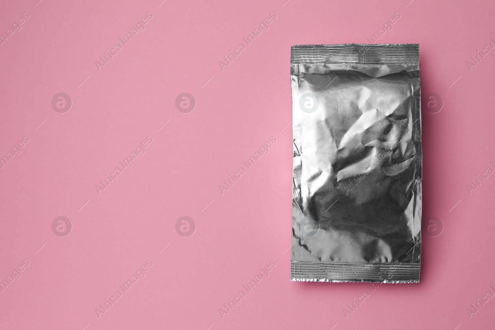 Photo of Blank foil package on pink background, top view. Space for text