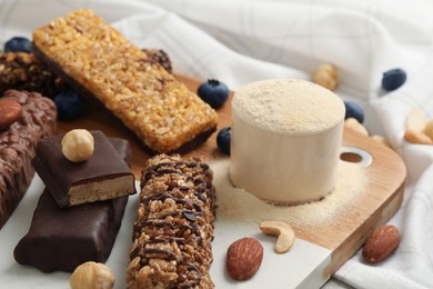 Photo of Different energy bars, nuts, blueberries and protein powder on table, closeup