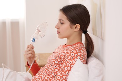 Cute girl holding nebulizer for inhalation on bed at home