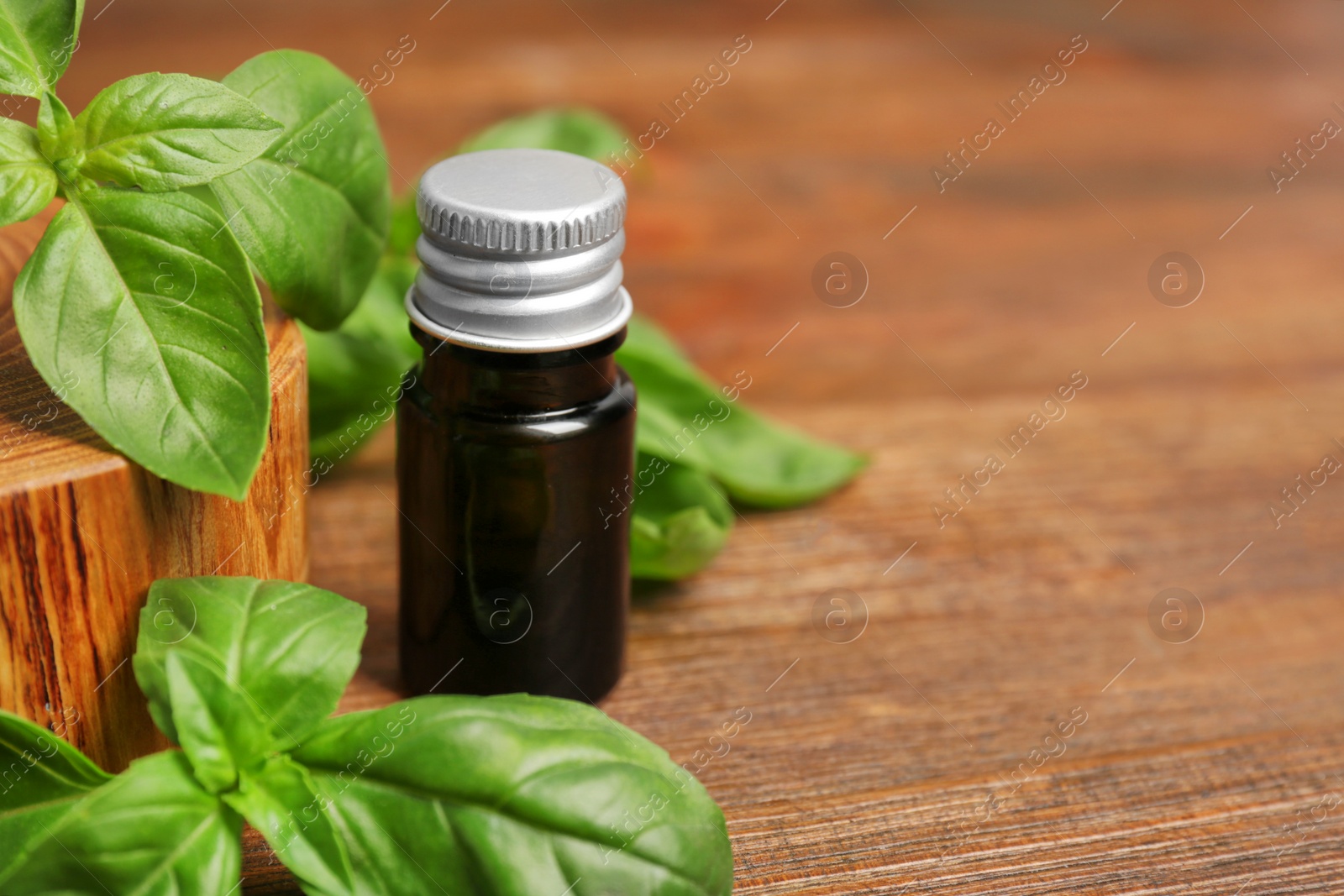 Photo of Glass bottle of basil oil with leaves and space for text on wooden table