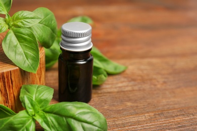 Glass bottle of basil oil with leaves and space for text on wooden table