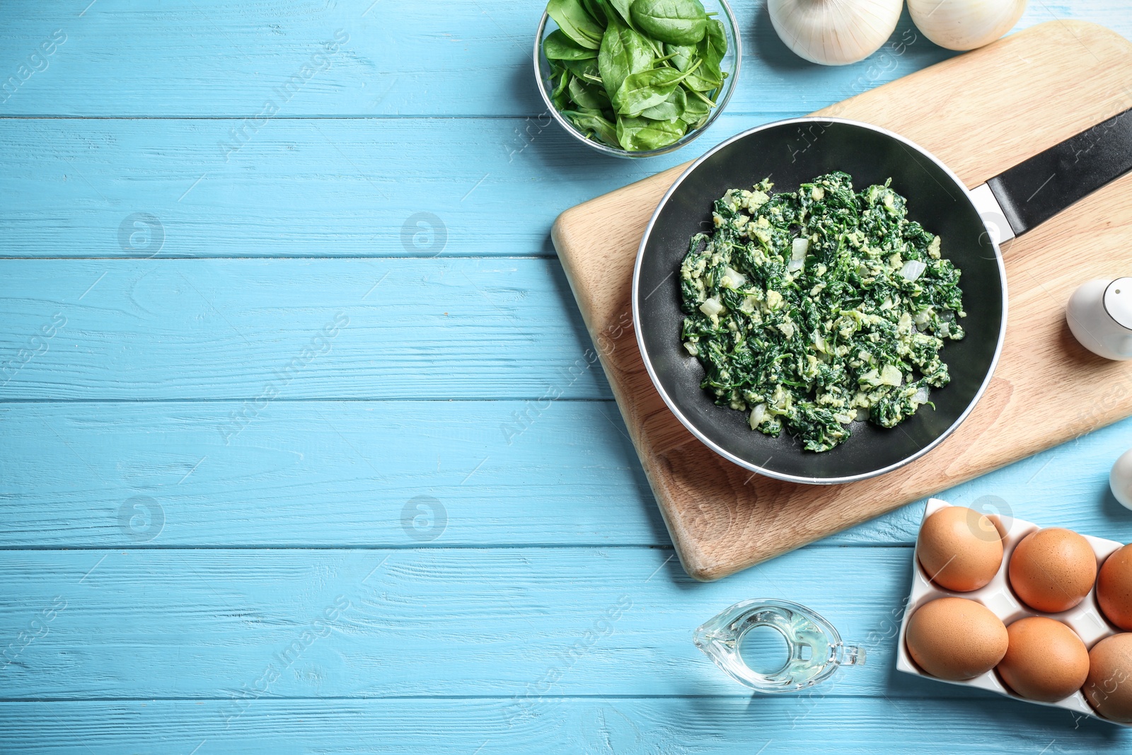 Photo of Flat lay composition of tasty cooked spinach and space for text on light blue wooden table. Healthy food