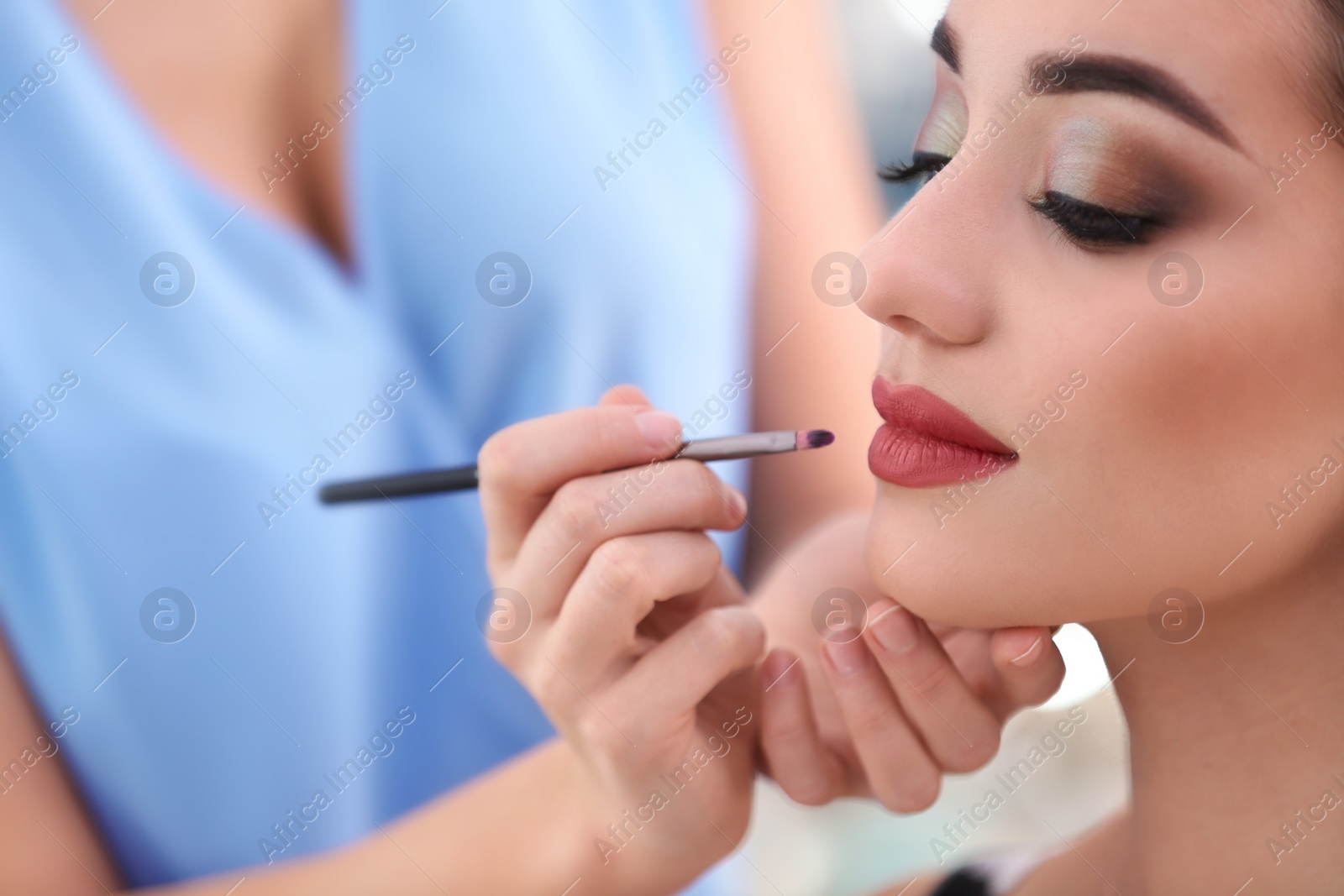 Photo of Professional visage artist applying makeup on woman's face in salon, closeup