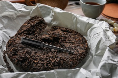 Photo of Broken disc shaped pu-erh tea and knife on parchment paper