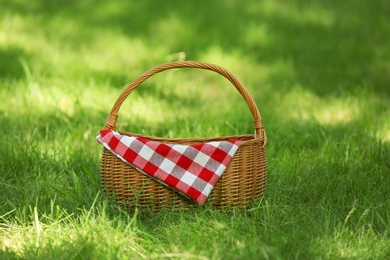Photo of Wicker basket with blanket on green grass in park. Summer picnic