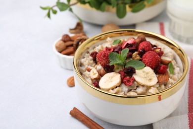 Photo of Delicious oatmeal with freeze dried berries, banana, nuts and mint on white table, closeup. Space for text