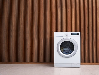 Photo of Washing machine with laundry near wooden wall. Space for text