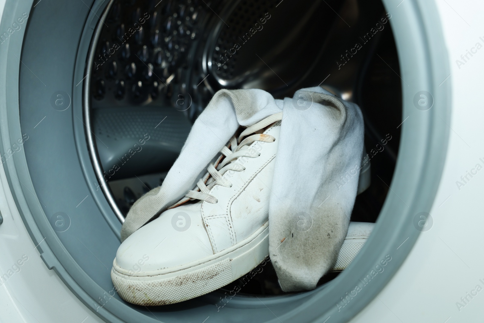 Photo of Sneakers with dirty socks in washing machine, closeup