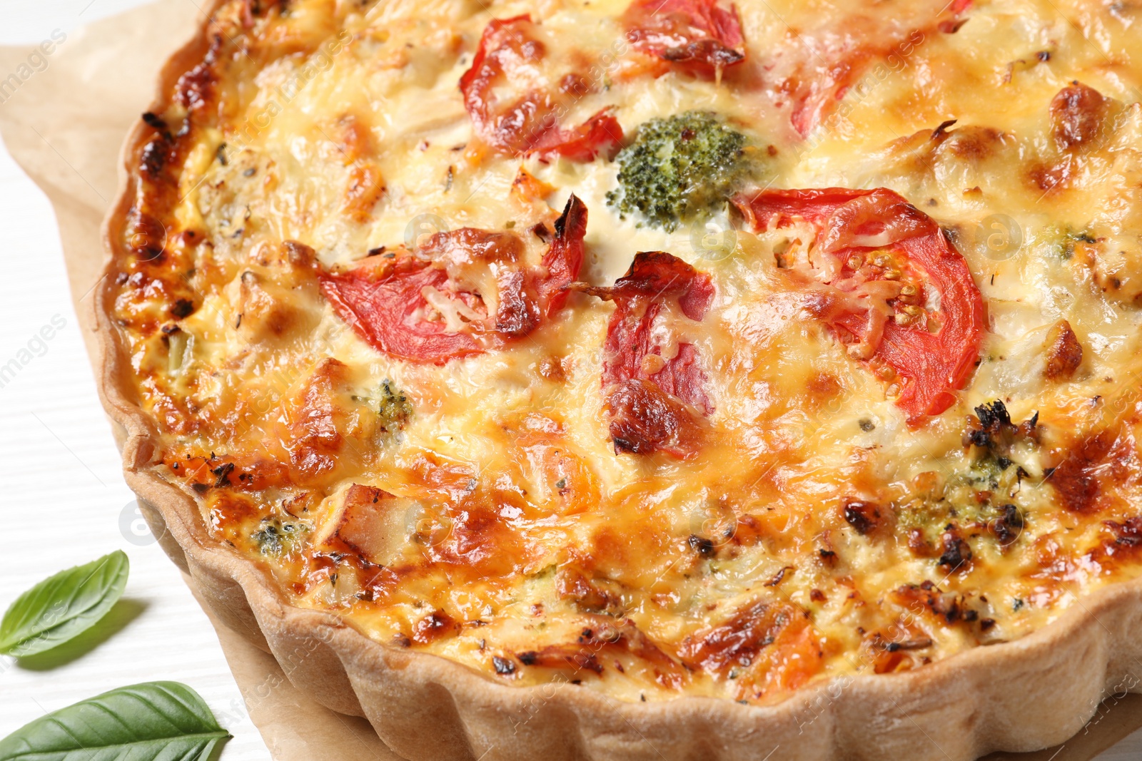 Photo of Tasty quiche with cheese, tomatoes and basil leaves on white wooden table, closeup