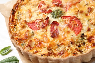 Tasty quiche with cheese, tomatoes and basil leaves on white wooden table, closeup