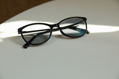 Photo of Stylish black eye glasses on white table. Space for text