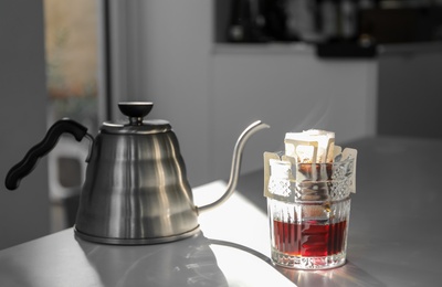 Photo of Glass with drip coffee bag and kettle on light grey table