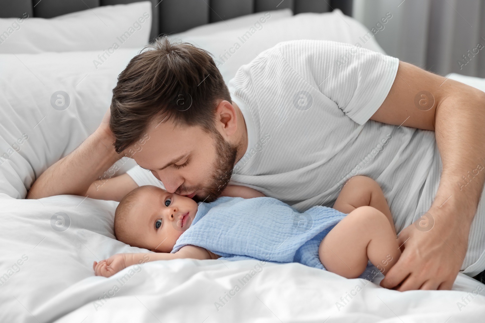 Photo of Father kissing his cute baby on bed indoors