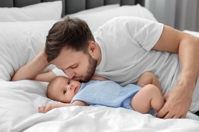 Father kissing his cute baby on bed indoors