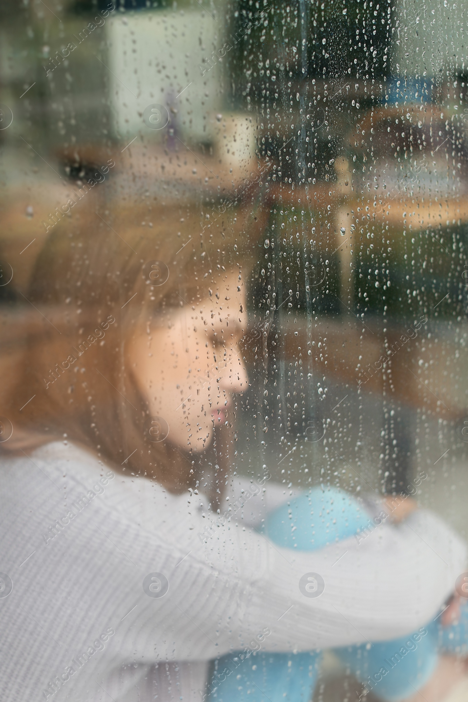 Photo of Depressed young woman near window, view from outside